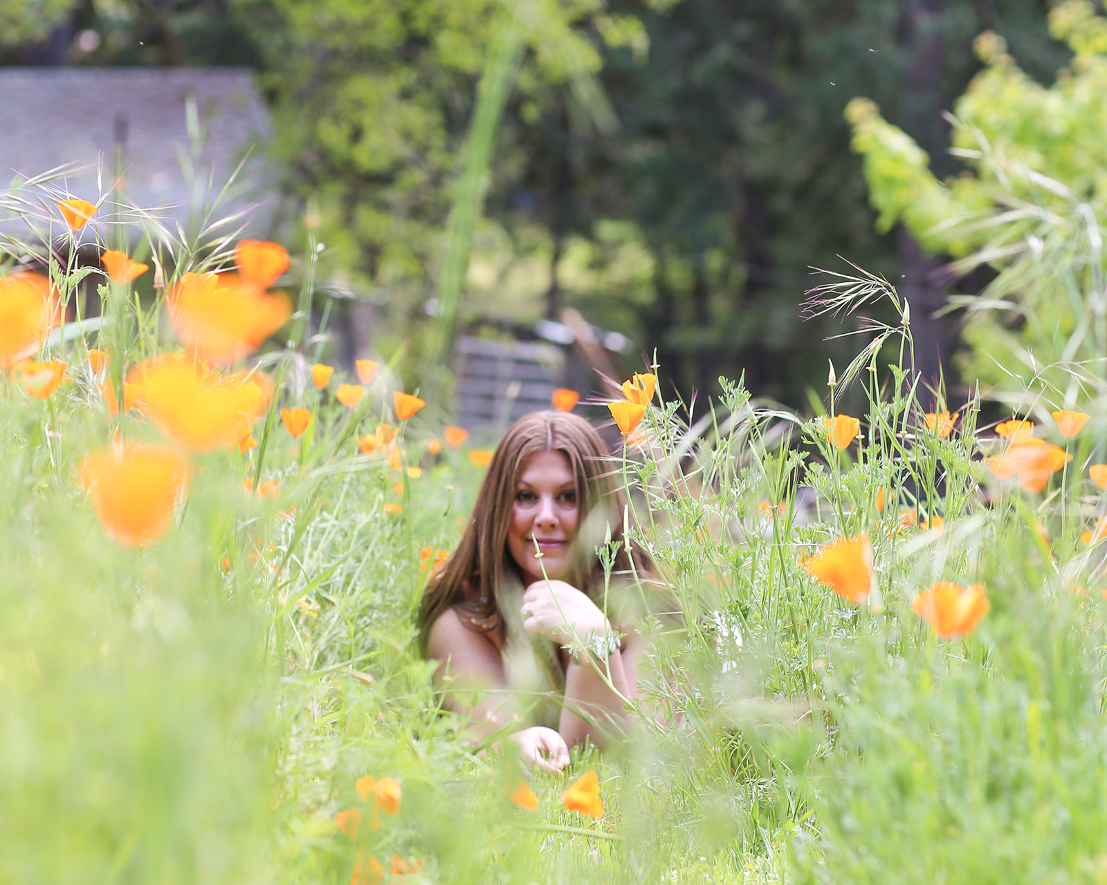 Amanda Smith of Body Whisper Healing sitting among orange wildflowers in a lush garden.