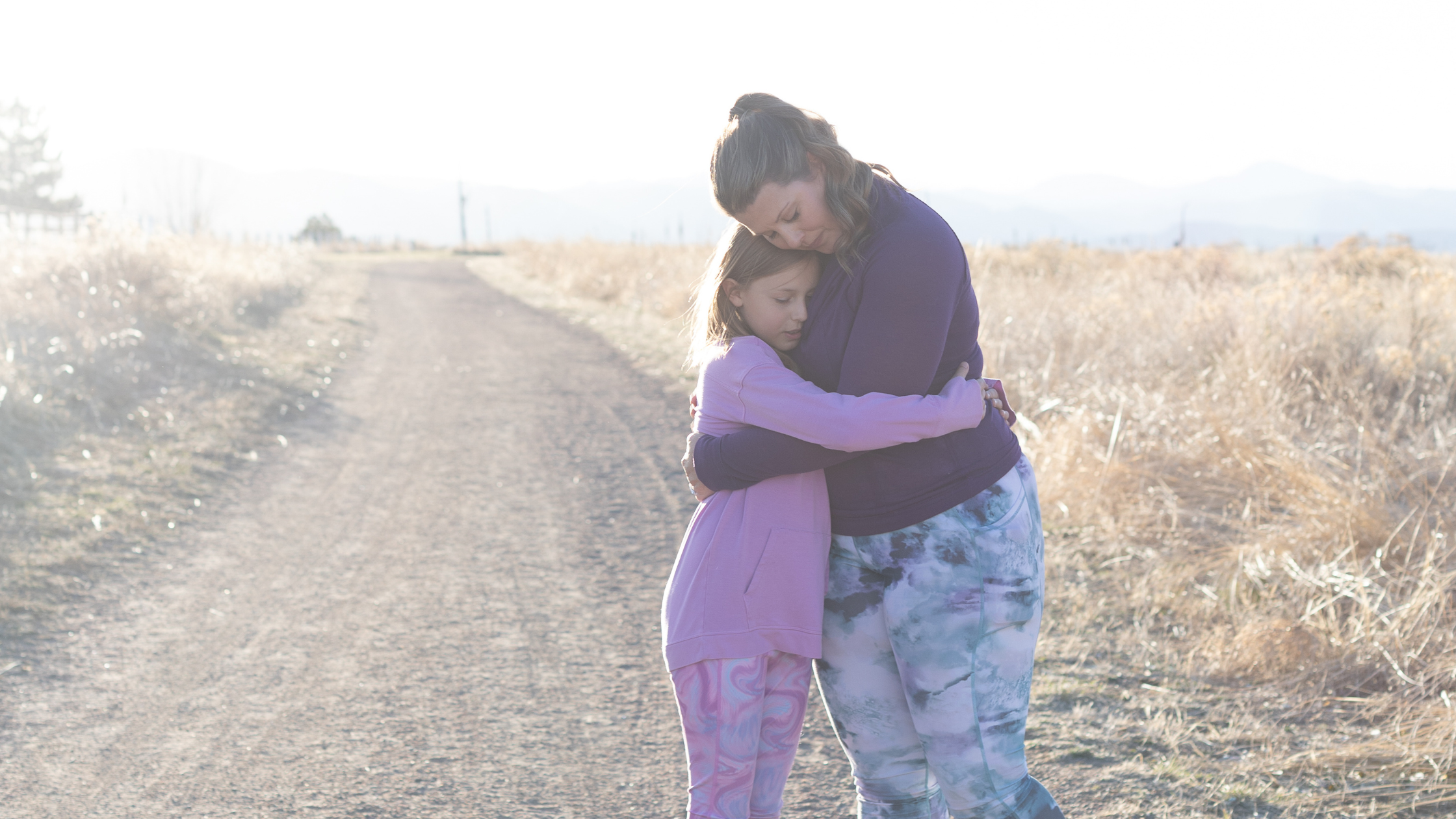Woman hugging a young girl outdoors, representing support and nervous system depletion in sensitive people.