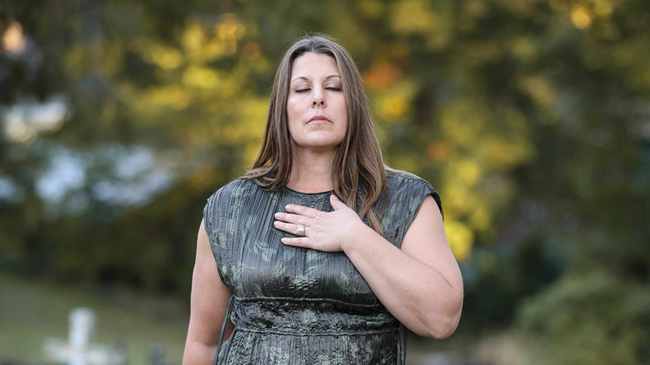 Amanda Smith standing outdoors with her eyes closed and one hand over her heart, taking a quiet moment to connect with her body.